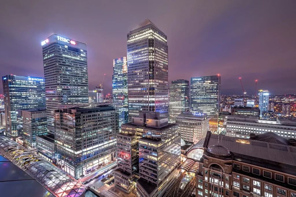 Canary Wharf banking towers lit at night, bank names visible on the skyline